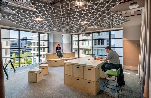 Two people work in a modern, light office space with timber workstations.